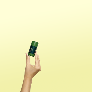 Hand holding the Outdoor Beauty Balm stick against a yellow background